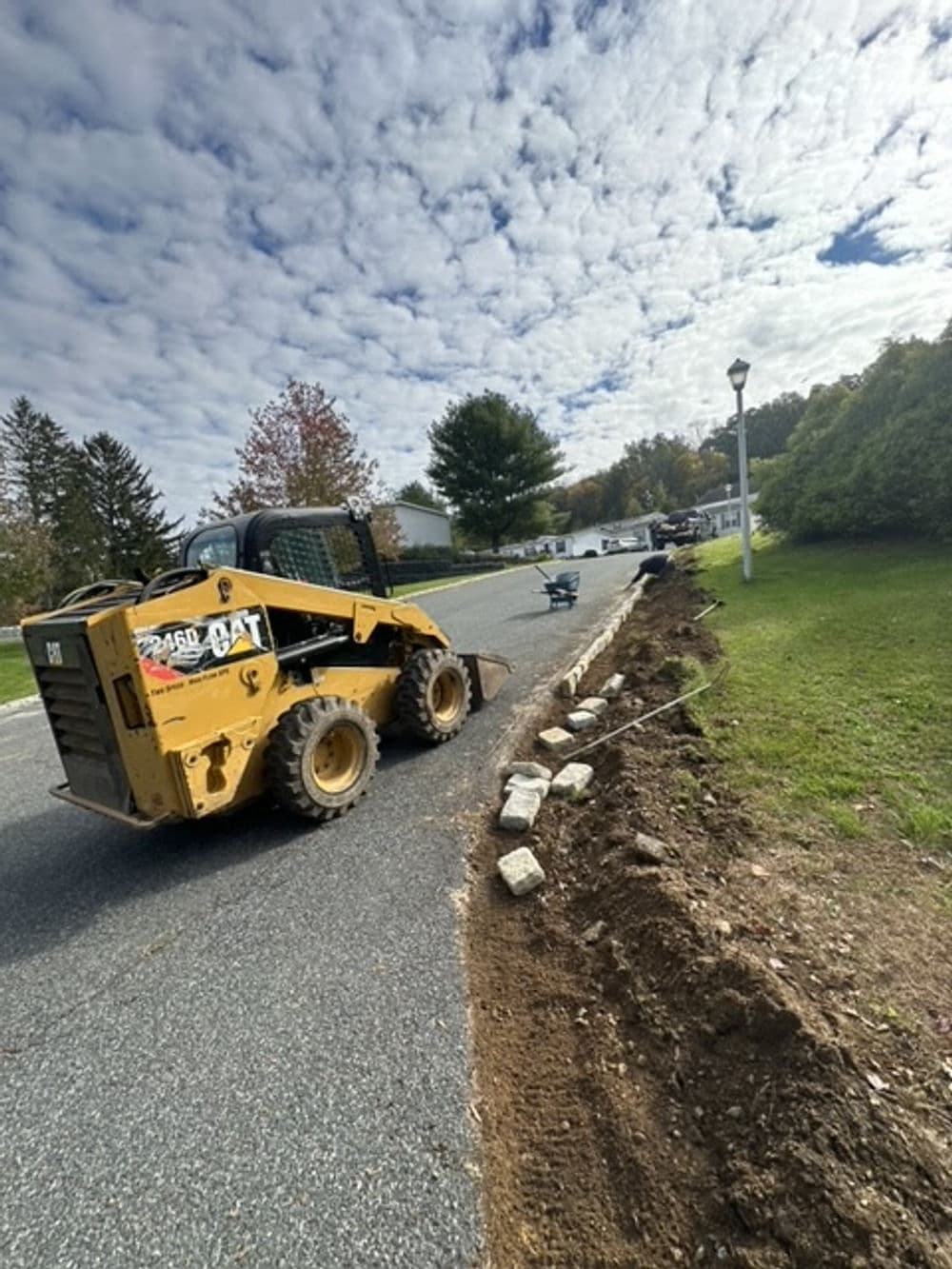 Skid steer loader working on road landscaping with stone edging and cloudy sky.