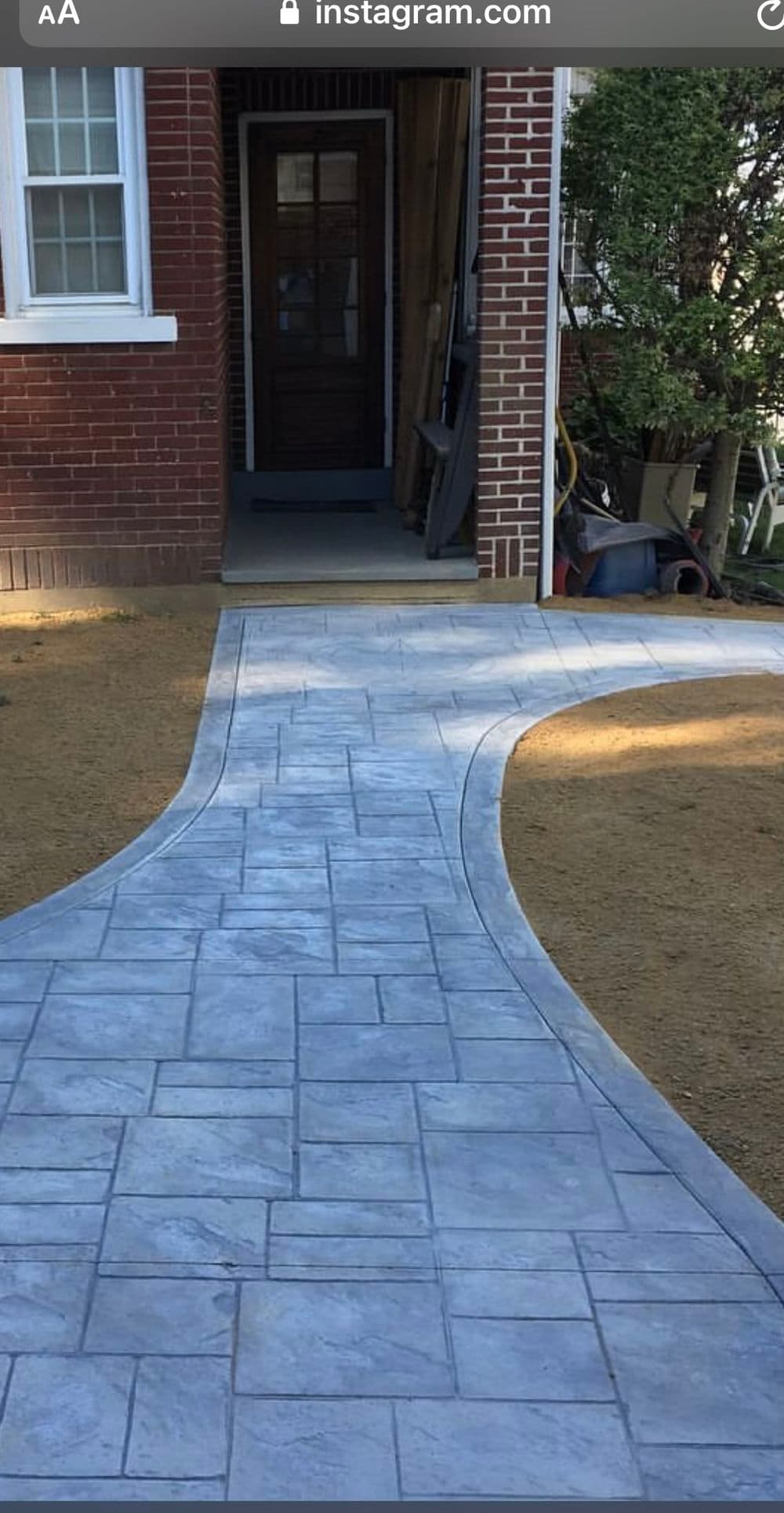 Patterned concrete walkway leading to a home's entrance, surrounded by grass and landscaping.