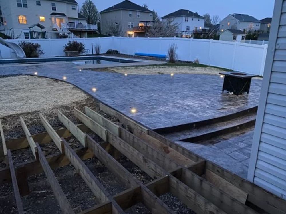 Backyard landscape with new stamped concrete patio, pool area, and unfinished wooden deck.