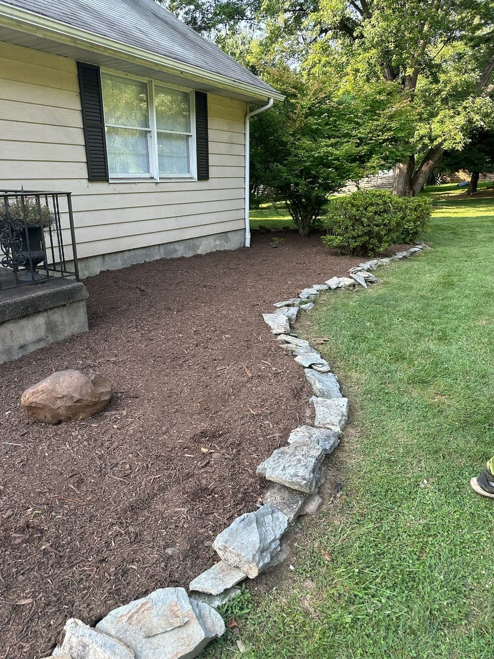 Landscaped yard with curved stone border, mulch, and shrubs beside a house.