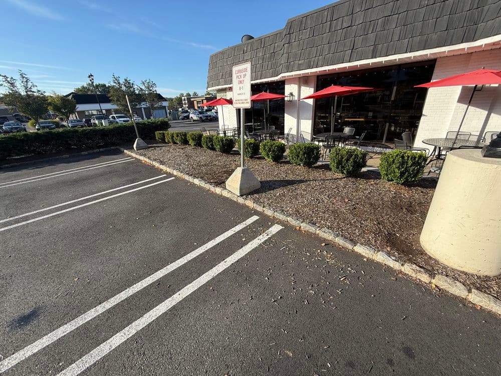 Empty parking lot with designated no parking sign and red umbrellas outside a restaurant.