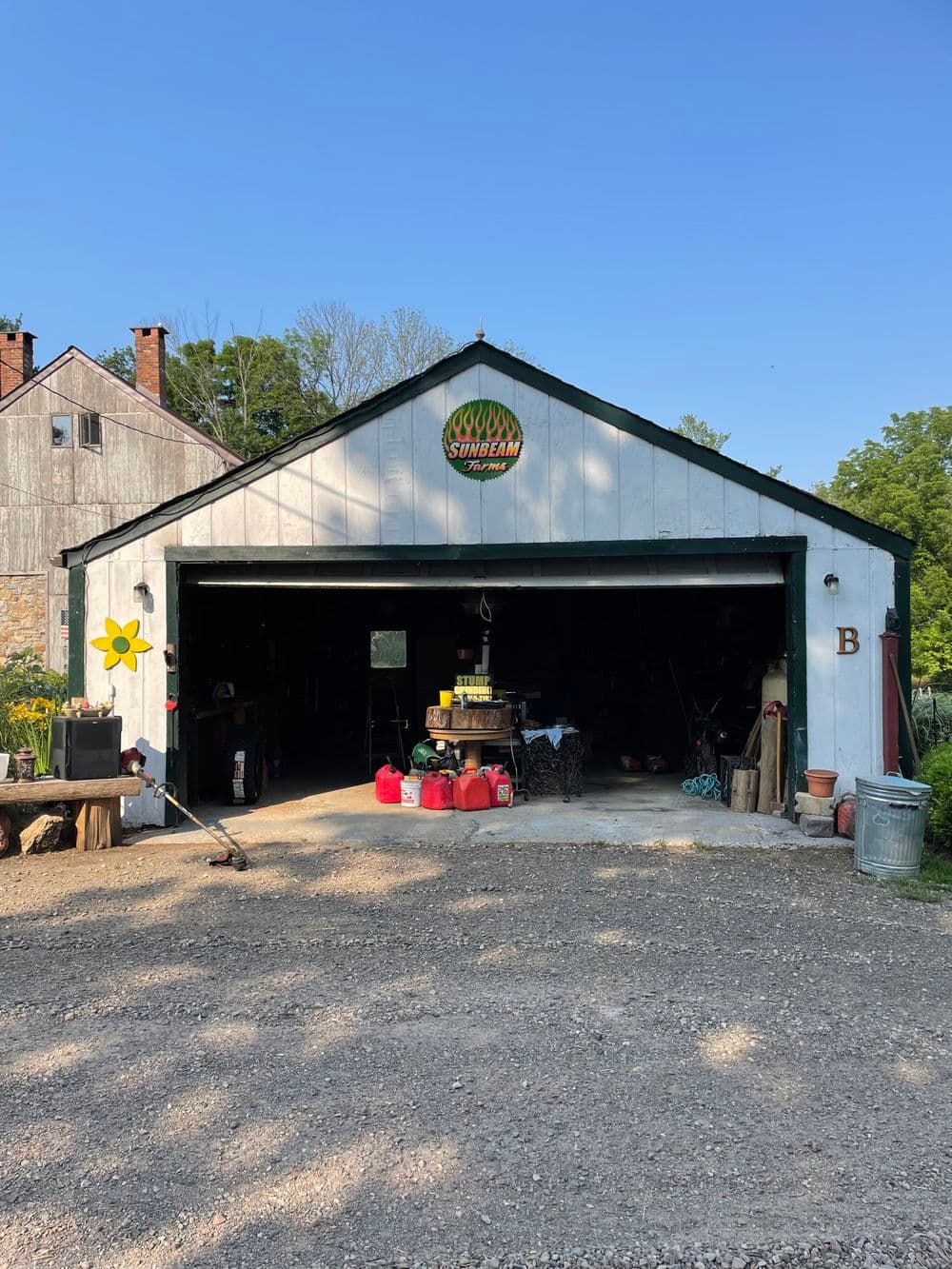Rustic barn garage with a green logo and flower decoration, set in a rural landscape.