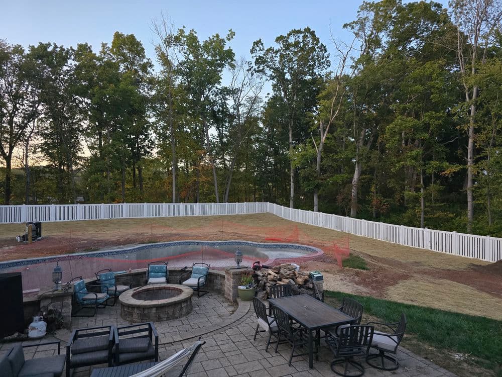 Backyard with a pool, patio area, and newly fenced lawn surrounded by trees.