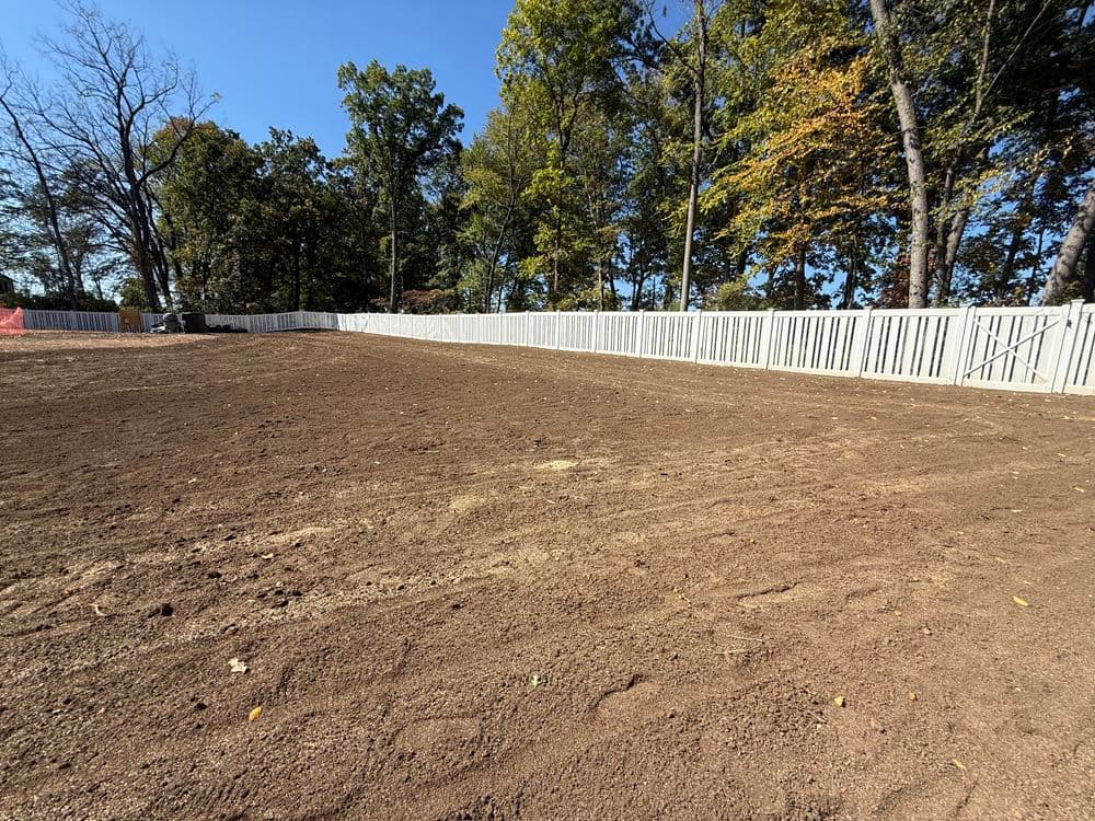 Cleared land ready for construction, surrounded by a white wooden fence and trees.