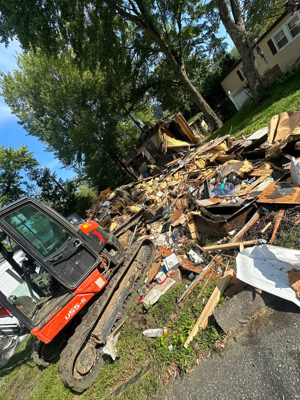 Excavator near debris from a demolished structure on a residential street.