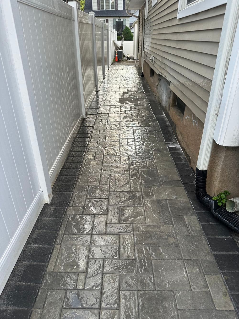 Paved walkway with decorative stone pattern between two fences beside a house.